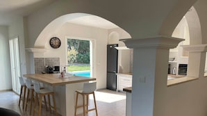 A modern kitchen with an island, bar stools, a large window, and an arched ceiling. - Nouveau : Très Jolie Villa Climatisée Avec Piscine (Puget-sur-Argens)