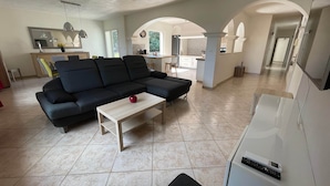 A spacious living area with a sectional sofa, a coffee table, and a modern kitchen in the background. - Nouveau : Très Jolie Villa Climatisée Avec Piscine (Puget-sur-Argens)