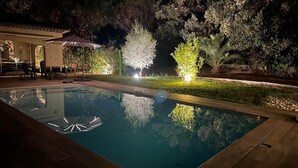 A nighttime pool area with a clear pool, surrounding greenery, and a covered seating area. - Nouveau : Très Jolie Villa Climatisée Avec Piscine (Puget-sur-Argens)