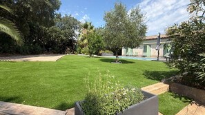 A well-maintained lawn with a pool area, surrounded by trees and a building with a tiled roof.