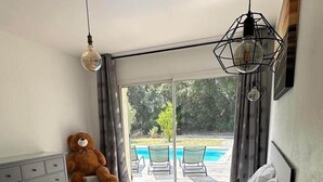 A bedroom with a bed, a teddy bear, a dresser, and a view of a swimming pool. - Nouveau : Très Jolie Villa Climatisée Avec Piscine (Puget-sur-Argens)