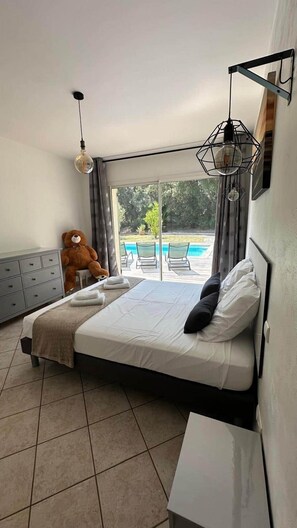 Una camera da letto con un letto, un orsetto di peluche, una cassettiera e vista su una piscina.