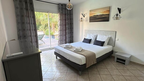 A modern hotel room with a large bed, a desk, and a view of the outdoors. - Nouveau : Très Jolie Villa Climatisée Avec Piscine (Puget-sur-Argens)