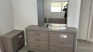 A bedroom with a wooden dresser, a mirror, and a small bedside table.