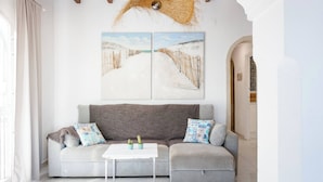 A living room with a grey sofa, a white coffee table, and two wall-mounted paintings depicting snowy landscapes. - Village La Gomera (Jávea)