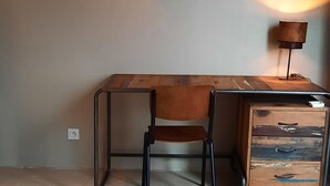 A room with a desk, chair, and a lamp. There is a painting on the wall.