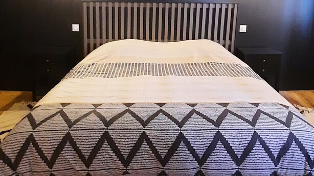 A bed with a patterned bedspread and a headboard, a wooden floor, and two wall-mounted lights.