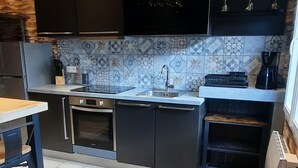 A modern kitchen with dark cabinetry, a tiled backsplash, and a dining area with a table and chairs.