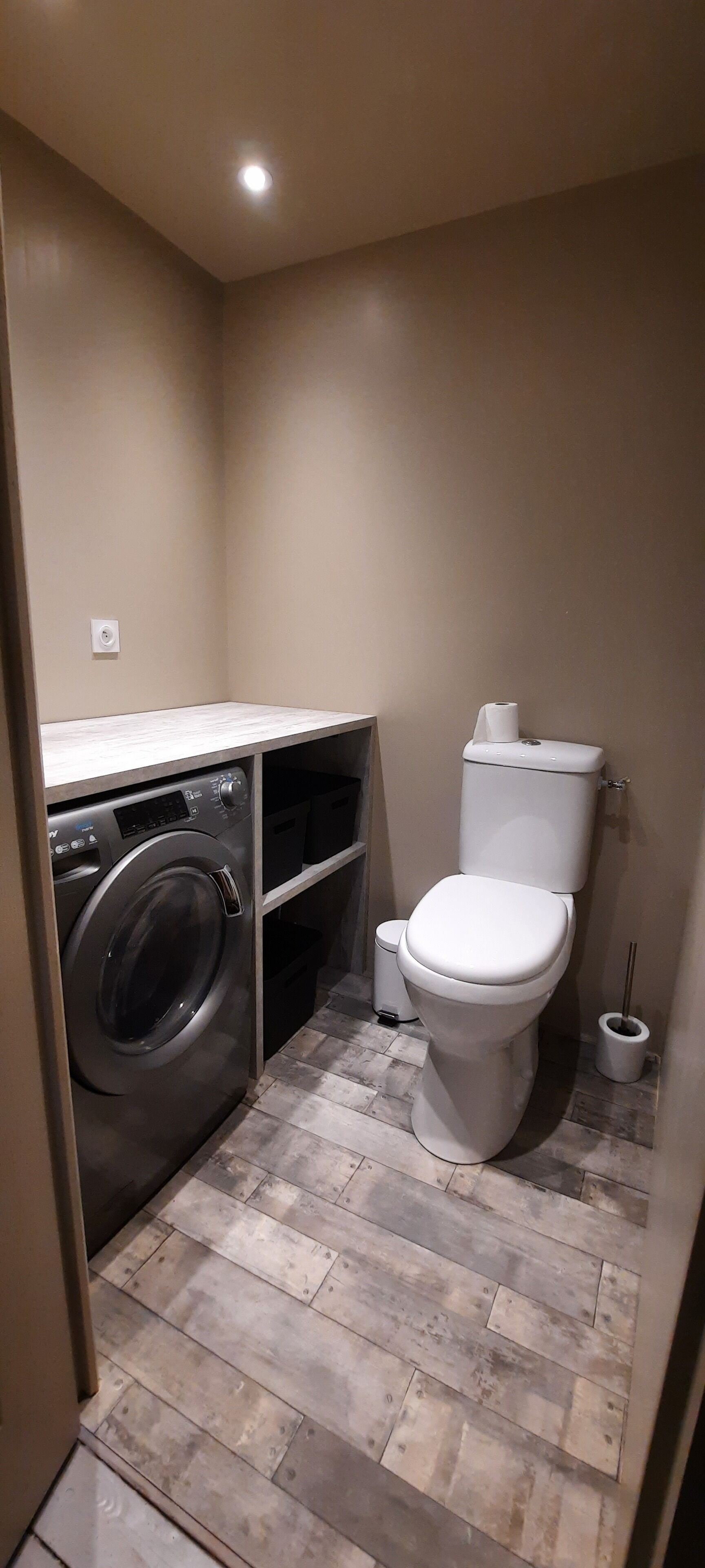 Een kleine badkamer met een wasmachine, toilet en een prullenbak.