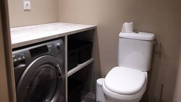 Een kleine badkamer met een wasmachine, toilet en een prullenbak.
