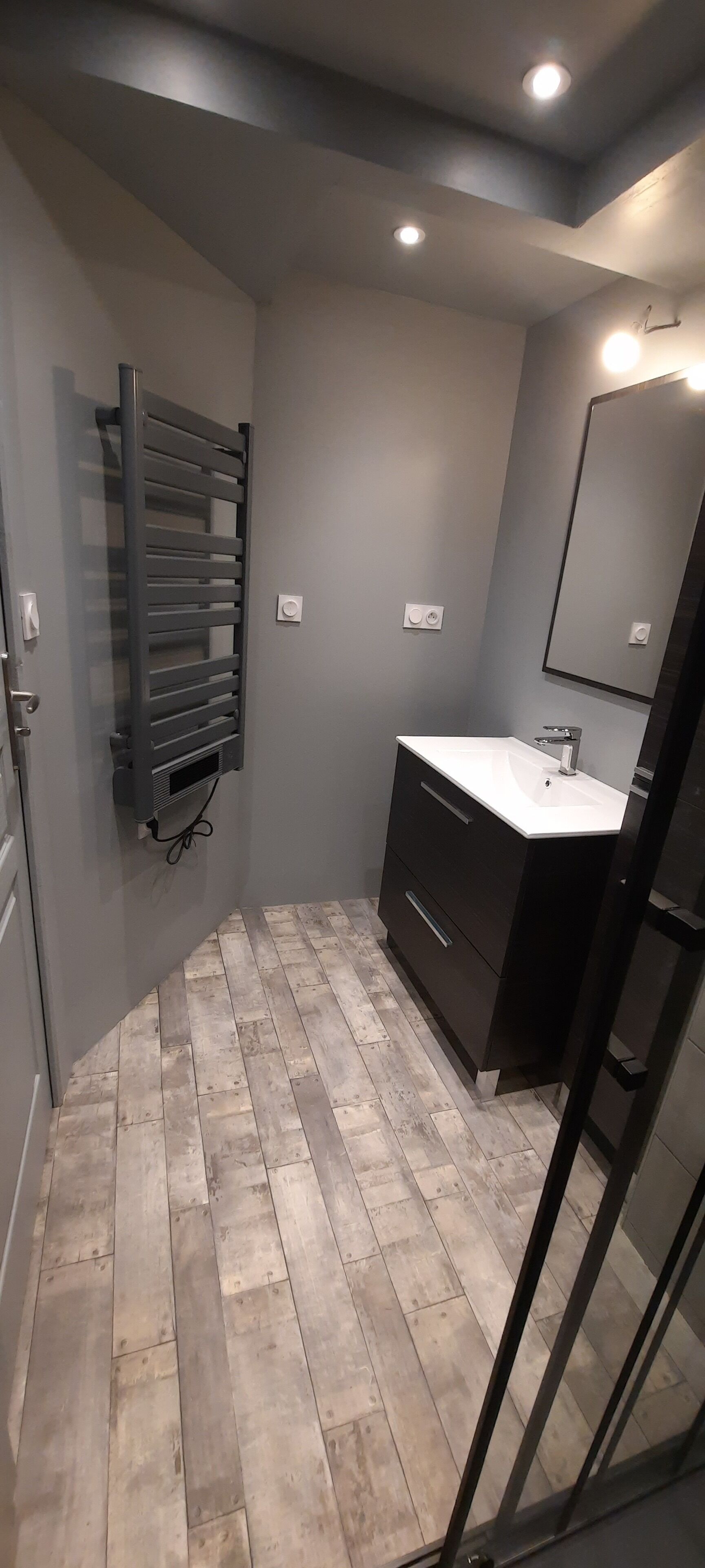 A bathroom with a grey tiled floor, a white sink with a mirror above it, and a towel rack on the wall.