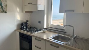 A compact kitchen with a gas stove, oven, and a sink with a view of the beach. - APARTMENT BY THE SEA (Roseto degli Abruzzi)