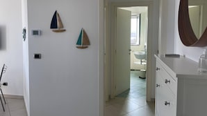 A hallway with a white wall, a door leading to a bathroom, and a mirror on the right. - APARTMENT BY THE SEA (Roseto degli Abruzzi)
