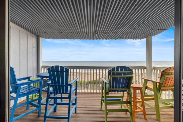 A covered outdoor deck with colorful Adirondack chairs and a view of the beach. - Blue Latitude - Oceanfront Condo (Carolina Beach)