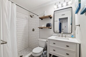 A modern bathroom with a shower, toilet, and vanity. - Blue Latitude - Oceanfront Condo (Carolina Beach)