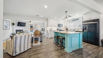 A modern kitchen with a large island, white cabinetry, and a stainless steel refrigerator.