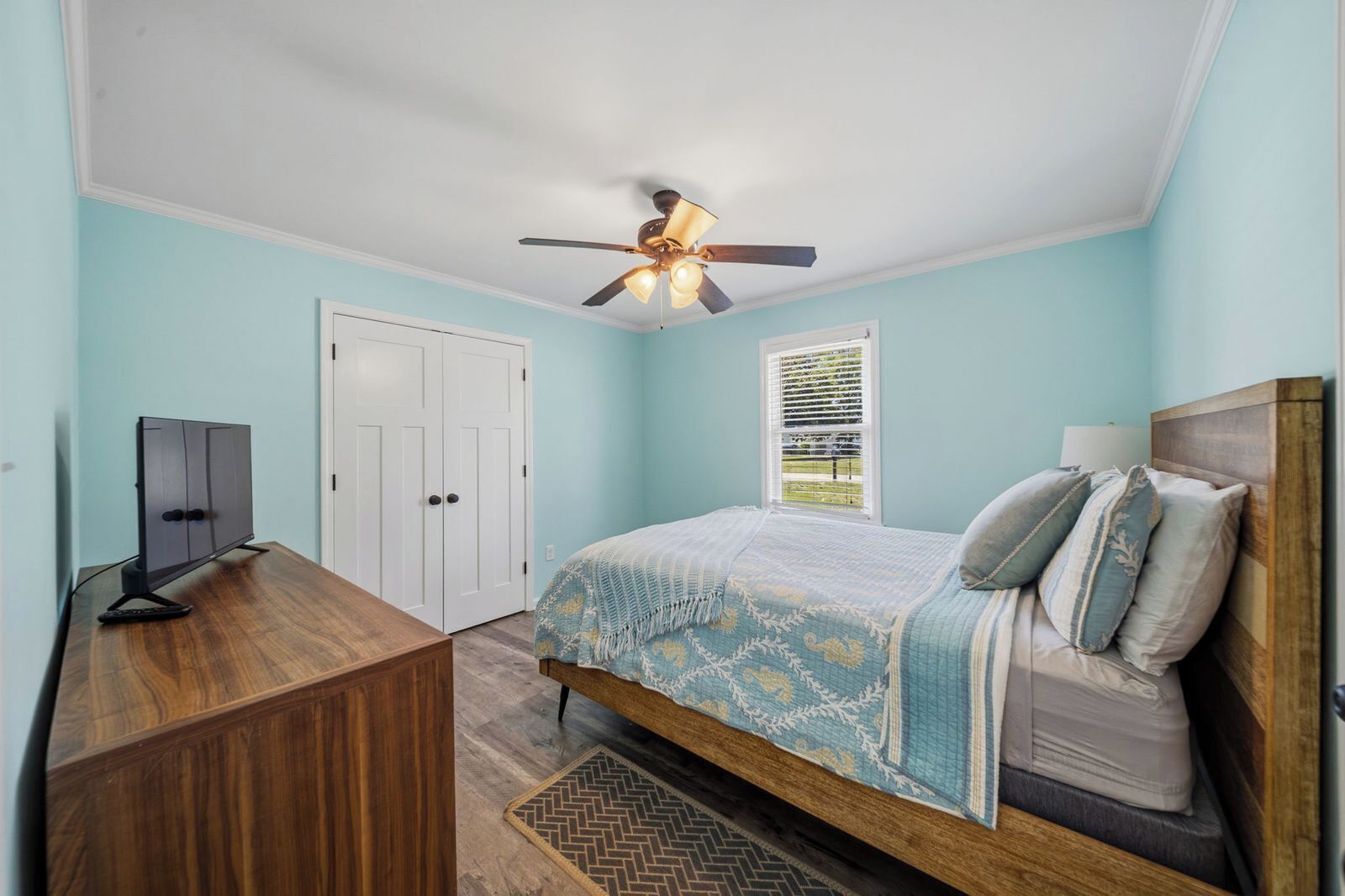 A bedroom with a bed, a desk, a ceiling fan, and a window with blinds.
