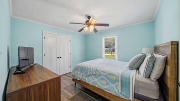 A bedroom with a bed, a desk, a ceiling fan, and a window with blinds.