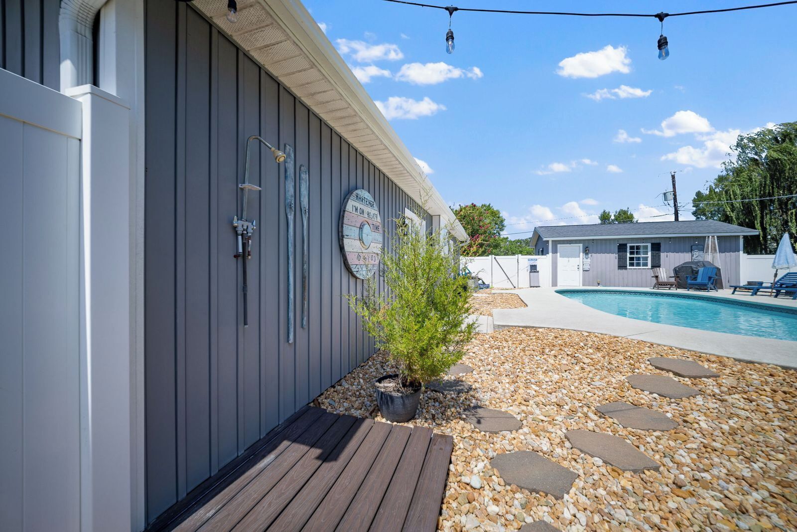 A poolside area with a wooden deck, a small shrub, and a stone pathway leading to a pool.