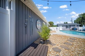 A poolside area with a wooden deck, a small shrub, and a stone pathway leading to a pool.