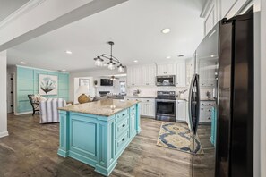 Una cocina con una isla grande, armarios blancos, electrodomésticos de acero inoxidable y una pared de acento color aguamarina.