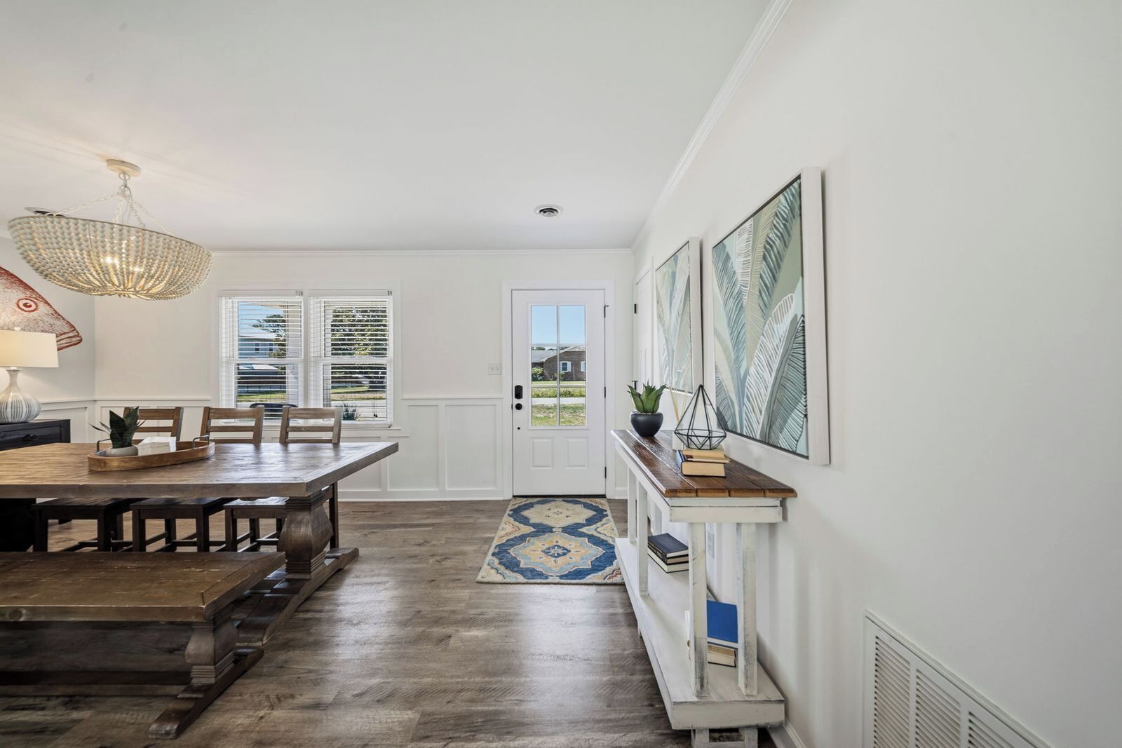 A dining area with a wooden table and chairs, a chandelier, and a view through a door to the outside.