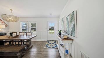 A dining area with a wooden table and chairs, a chandelier, and a view through a door to the outside.