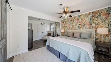 A bedroom with a bed, a ceiling fan, a nightstand, a lamp, a chair, and a door leading to another room.