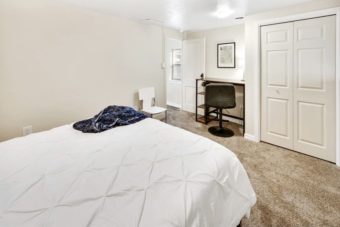 A bedroom with a bed, a chair, a desk, and a wardrobe.