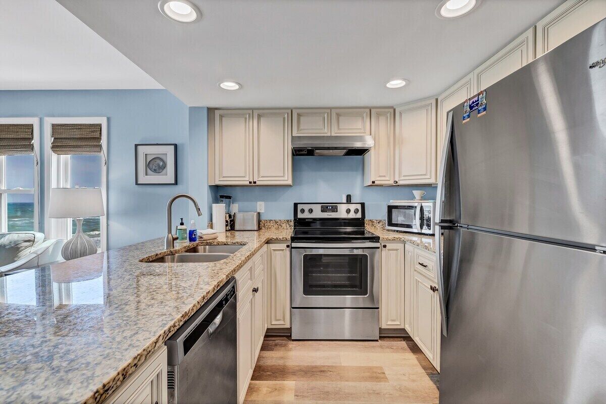 A modern kitchen with light-colored cabinets, stainless steel appliances, and a granite countertop.
