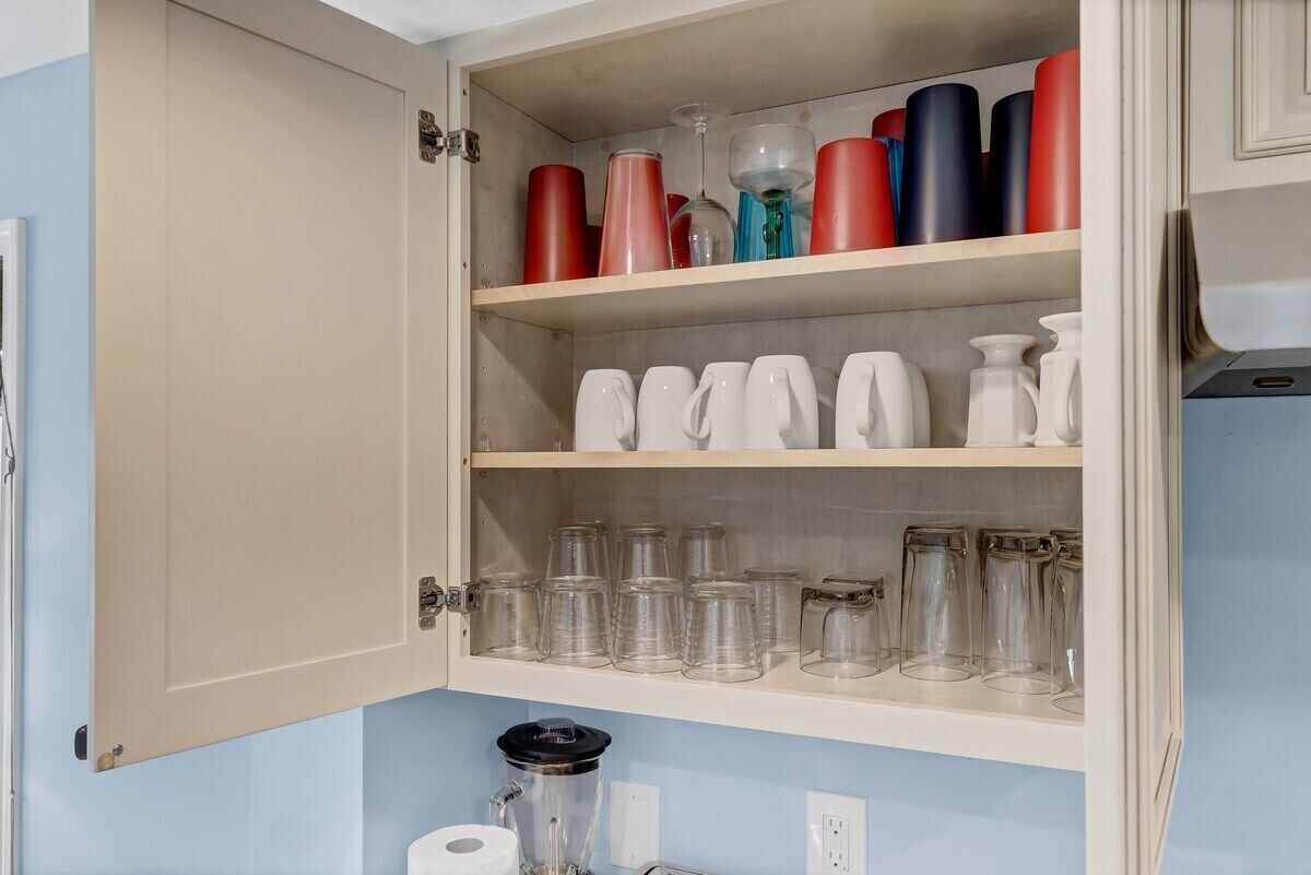 A kitchen cabinet with shelves holding various glassware and containers.