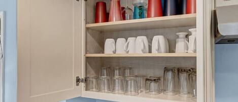 A kitchen cabinet with shelves holding various glassware and containers.
