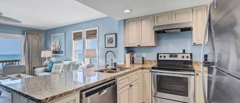 A modern kitchen with stainless steel appliances, a granite countertop, and a view of the ocean.