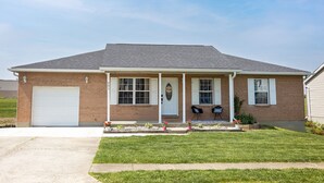 A single-story brick house with a white garage door, a front porch with two chairs, and a small garden with flowers. - 4 Bed, 2.5 Bath, 3 KING BEDS on a Private Lake with Dock! Family Friendly (Crittenden)