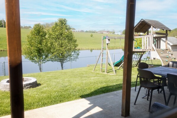 A patio with a swing set and a wooden playhouse by a body of water.