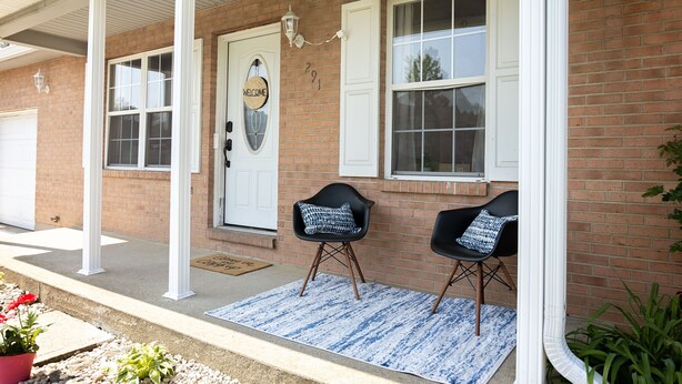 A brick house with a white front door, two black chairs with patterned cushions, and a blue and white rug on the porch. - 4 Bed, 2.5 Bath, 3 KING BEDS on a Private Lake with Dock! Family Friendly (Crittenden)