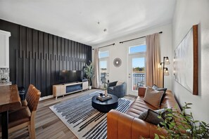 Una sala de estar moderna con un televisor de pantalla plana, un sofá, una mesa de centro y un comedor con sillas.