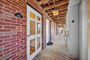 A corridor with a brick wall, a white door with glass panels, and a wooden ceiling.