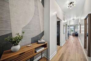 A modern hallway with a wooden console table, a potted plant, and a wall with a geometric design.