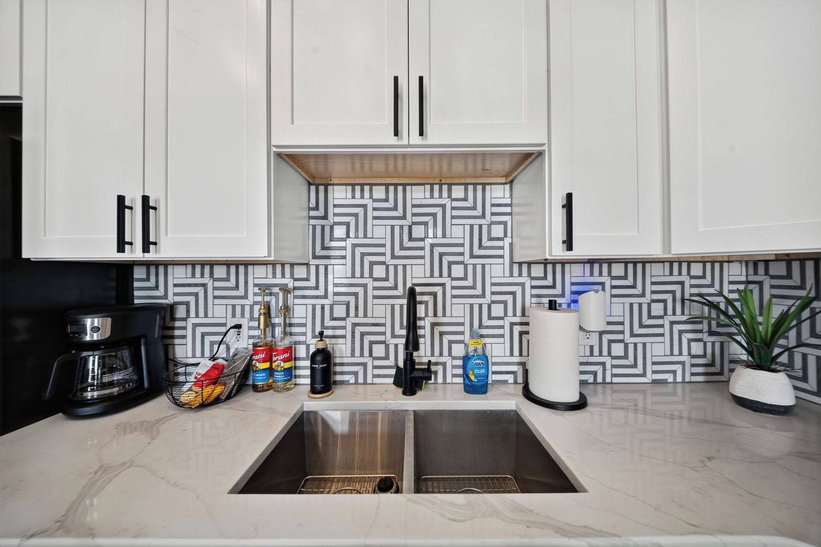 A kitchen with white cabinets, a marble countertop, and a geometric backsplash.