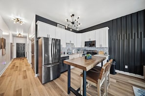 A modern kitchen with stainless steel appliances, a wooden dining table, and a black accent wall.