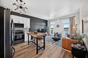 A modern kitchen with a dining area, a living room with a sofa and a TV, and a balcony with a view.