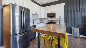 A modern kitchen with white cabinets, stainless steel appliances, a wooden table, and yellow bar stools.