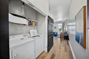 A laundry area with a washing machine and dryer, a shelf with cleaning supplies, and a door leading to a balcony.