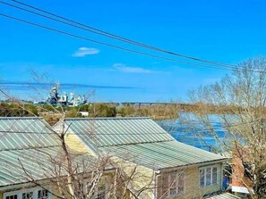 Un edificio costero con techo metálico, vista al mar y un puente al fondo.