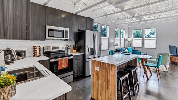 A modern kitchen with a central island, stainless steel appliances, and a large window overlooking greenery. - Modern Flat - Downtown (Wilmington)