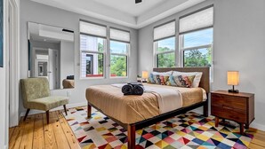 A bedroom with a bed, a chair, a nightstand, and a colorful geometric rug. - Modern Flat - Downtown (Wilmington)