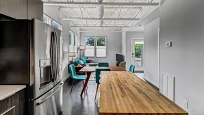 A modern kitchen with a large wooden table, stainless steel appliances, and teal chairs. - Modern Flat - Downtown (Wilmington)