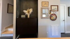 A hallway with a dark-colored reception desk, a decorative vase with feathers, framed artwork, and a wall-mounted thermostat.