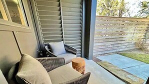 A balcony with wicker furniture, a small wooden table, and a view of a wooden fence and greenery.